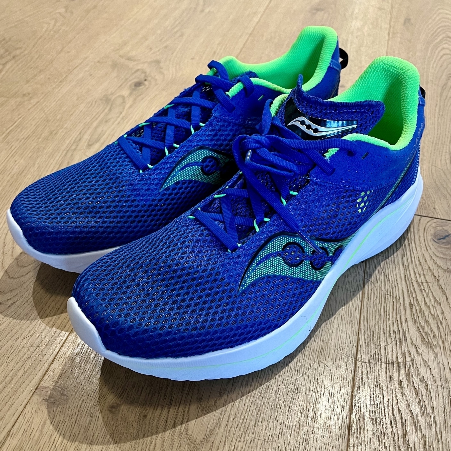 A pair of blue running shoes with neon green interior rests on a wooden floor.